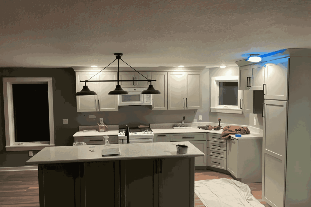 Modern kitchen with white cabinets, an island, pendant lights, and a dark accent wall. Countertops display various items; a towel and cloth rest on the right counter, with a sheet on the floor—ideal for showcasing top-notch electrical services.