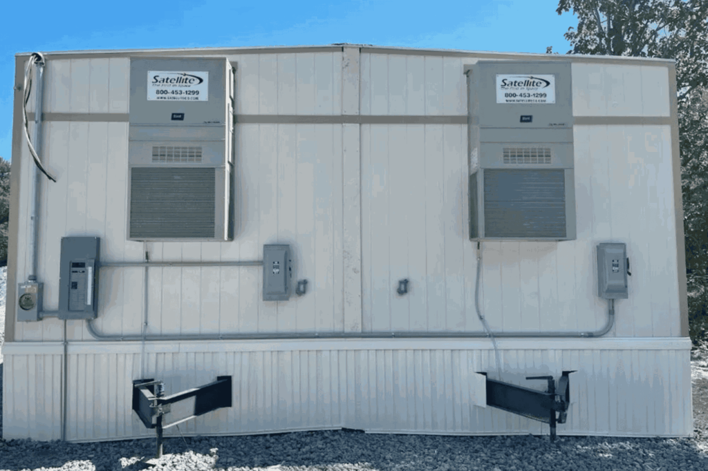 Two air conditioning units are mounted on the exterior wall of a mobile building, with electrical panels and support brackets below each unit—ideal for showcasing the quality work of an electrical contractor or electrician service in Angola.