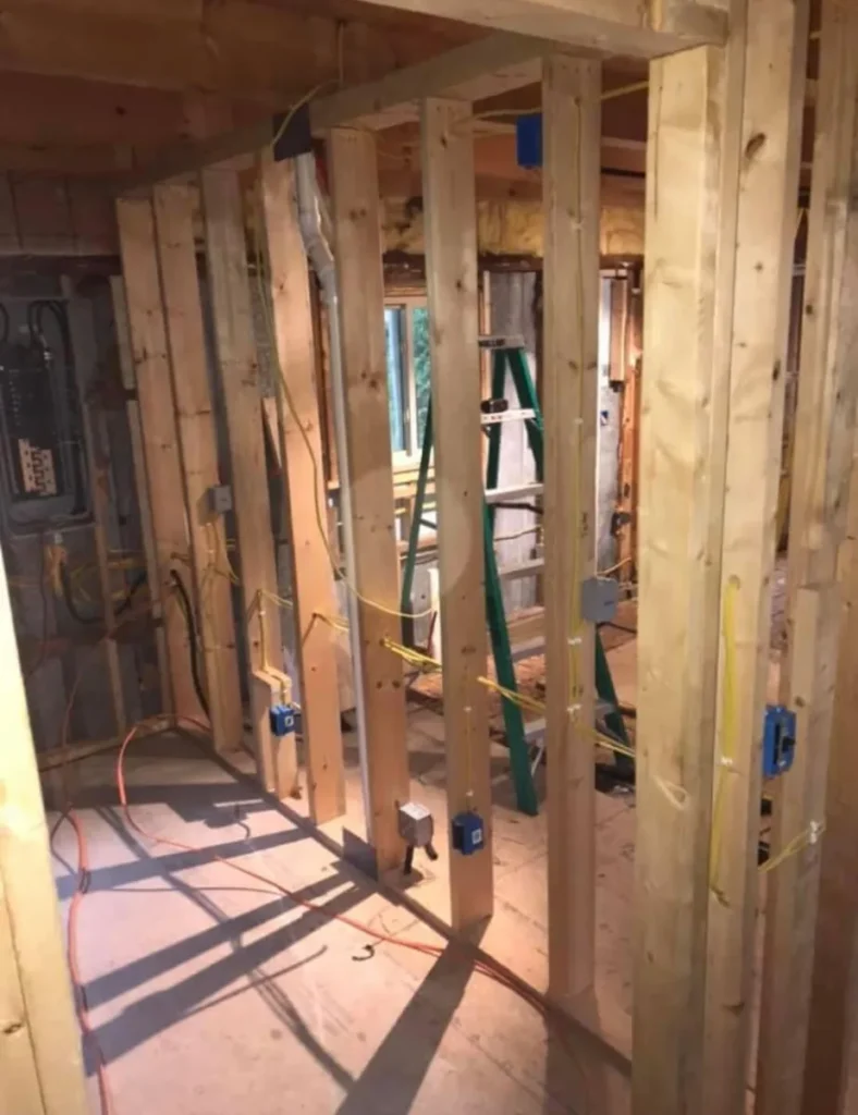 Wood framing for interior walls with electrical wiring and outlet boxes installed by an experienced electrical contractor; a ladder and unfinished walls visible in the background inside a building under construction.
