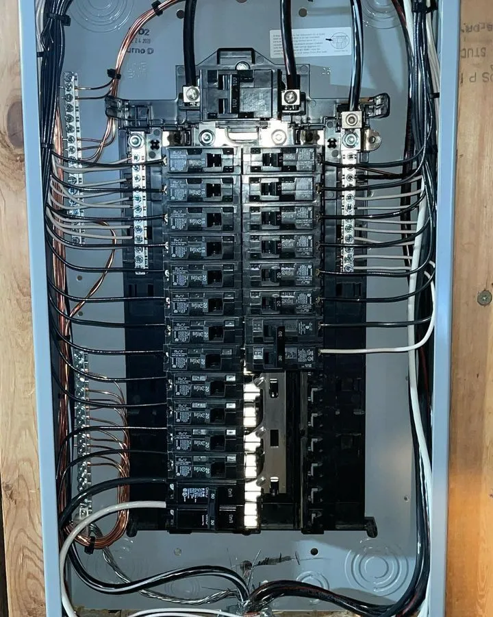 An electrical breaker panel with multiple circuit breakers, neatly organized black and white wires, and grounding wires connected on the sides.