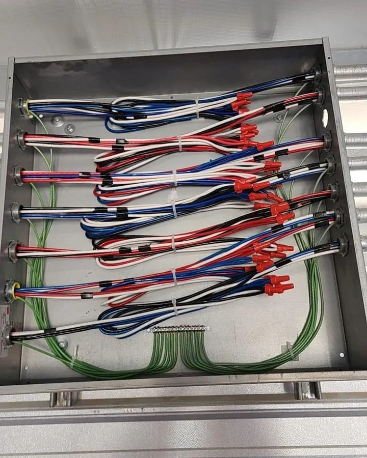 A metal electrical panel with organized red, blue, black, and green wires, connected and secured with zip ties and red wire connectors.