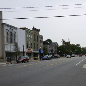 A small town main street with parked cars, historic buildings, trees, and a distant church steeple under an overcast sky—an ideal setting for a trusted electrical contractor or Electrician Service in Angola to keep the lights shining.