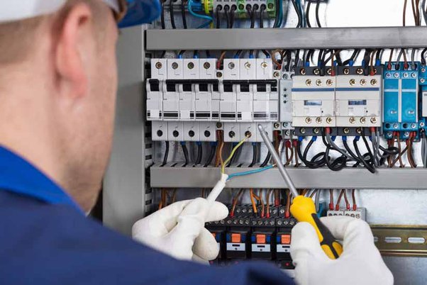 An electrician wearing gloves uses a screwdriver and probe to work on electrical wiring inside a control panel, showcasing precise electrical repair and top-notch electrician services in Auburn.
