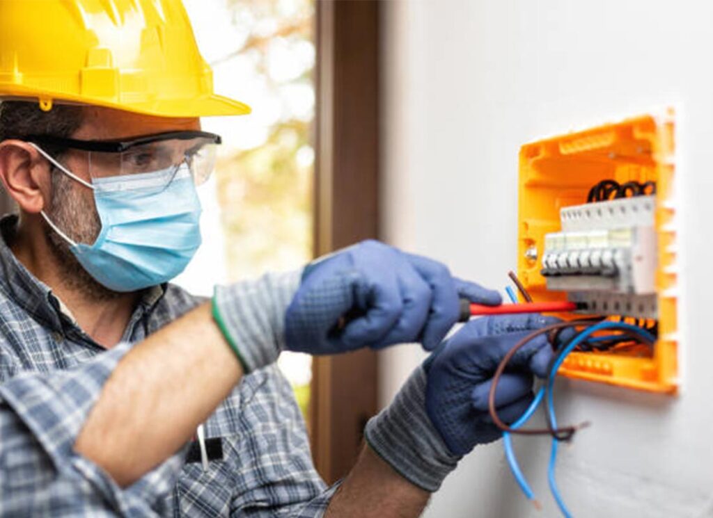 A man wearing a mask and gloves works on an electrical box, showcasing professional electrical repair expertise.