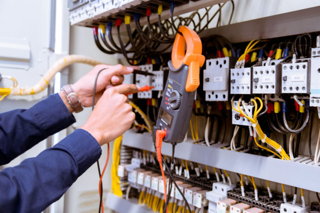 Hands using a digital multimeter to test electrical connections inside an open control panel, showcasing precise Electrical Repair as part of professional electrician services in Huntertown.